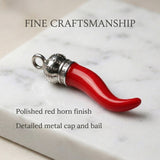 Red horn-shaped pendant with silver cap on a marble surface, text highlighting 'Fine Craftsmanship'.