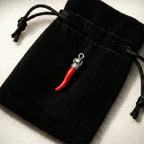 Red chili pepper-shaped pendant with silver top on a black drawstring bag.