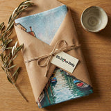 Gift wrapped in brown paper with scenic images and 'P.S. I Love Italy' tag on a wooden surface.
