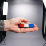Hand holding a small rectangular object with red, white, and blue colors against a neutral background